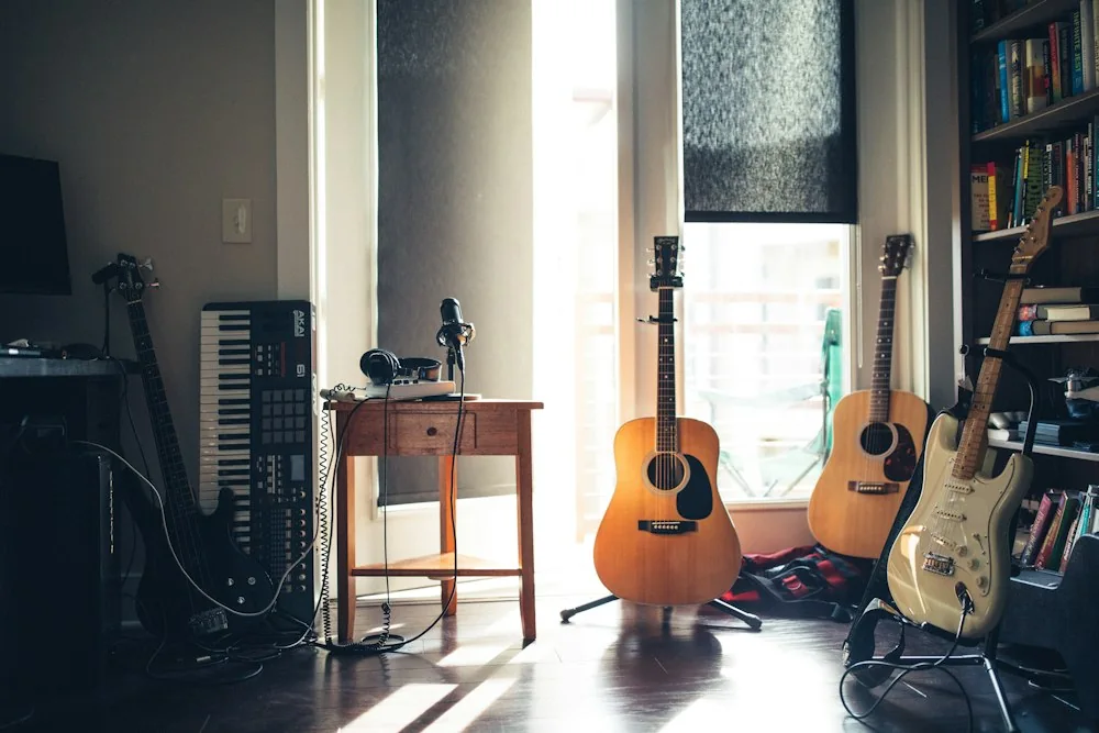 Guitars and a keyboard beside a sunlit window and bookshelves
